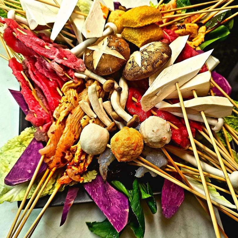 Assortment of raw meats, mushrooms, and vegetables on skewers, ready for hot pot or grilling.