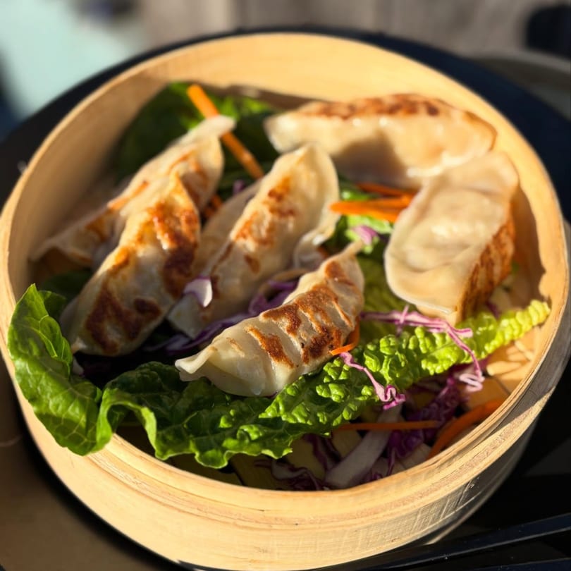 Pan-fried dumplings with lettuce, shredded carrots, and purple cabbage in a bamboo steamer.